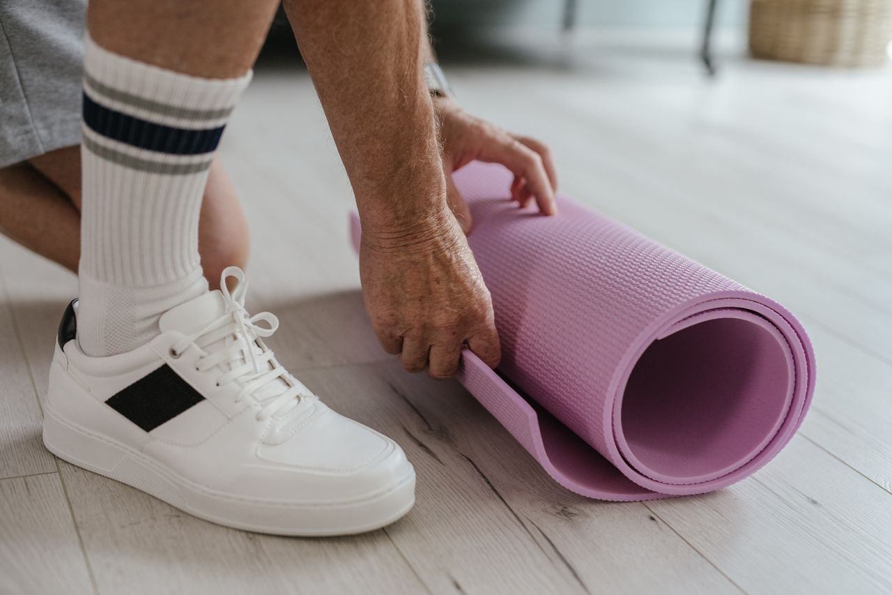 Home Close-up of a person rolling a pink yoga mat on a light wooden floor, wearing white sneakers.
